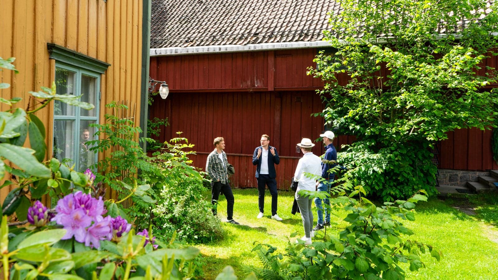 Guidet tur i trehusbebyggelse med fire gutter i en fin hage med blomster