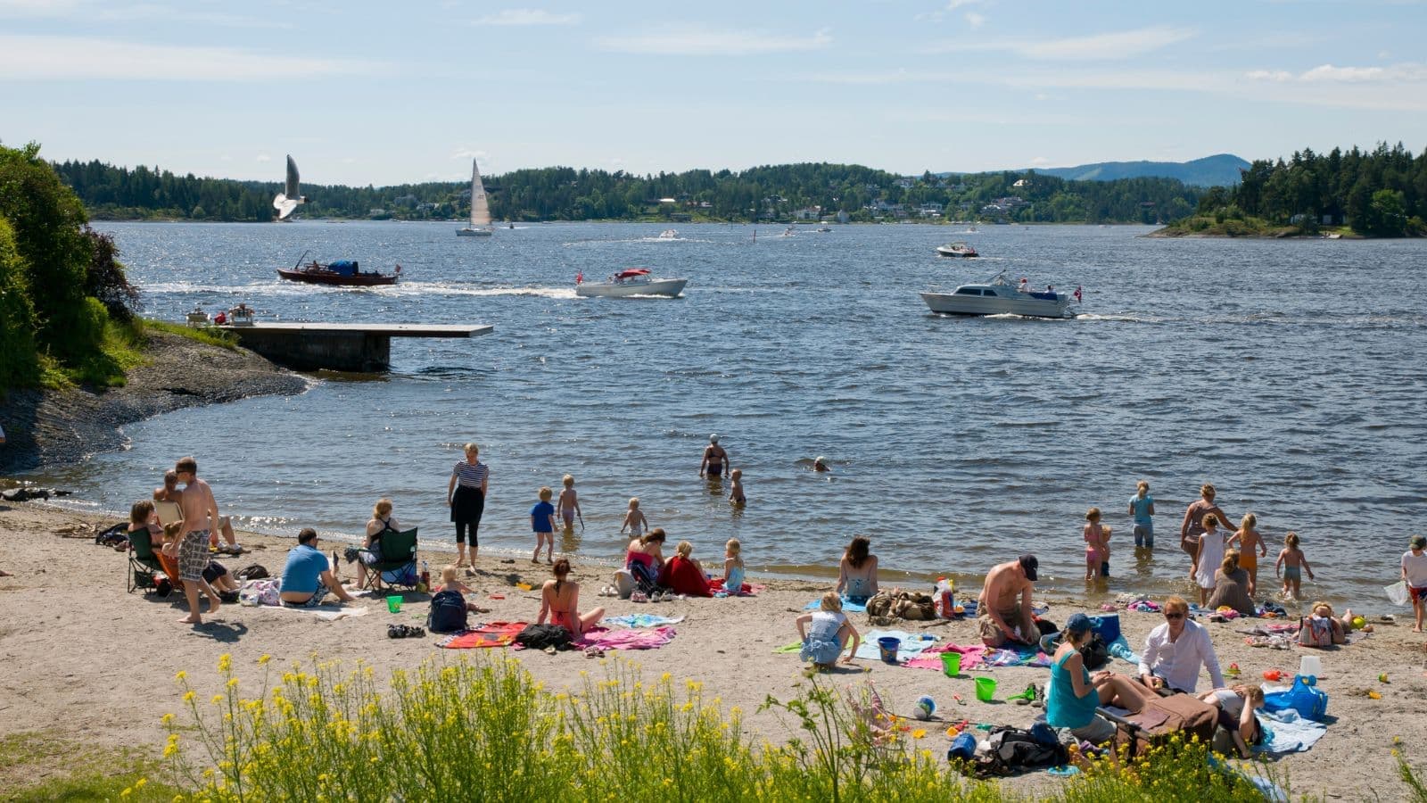 Folk som koser seg i sola på en liten strand båter kjører på. vannet i bakgrunnen