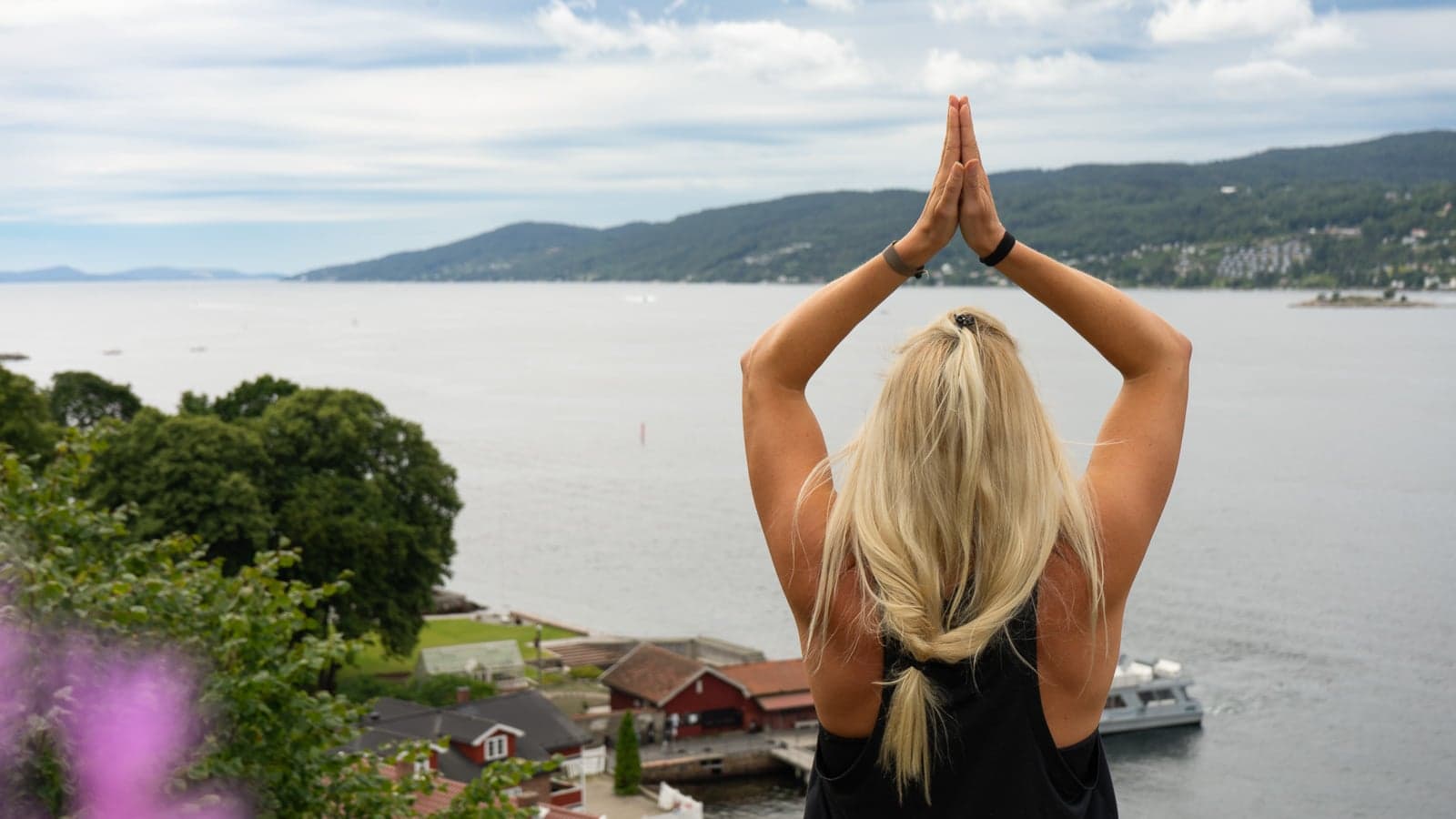 Dame som gjør yogaposering ved utsiktspunkt utover fjorden