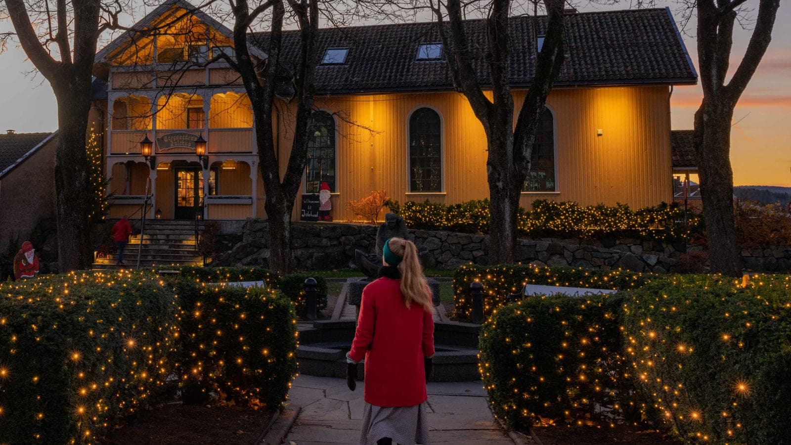 Dame som går utenfor et gult trehus i juletider